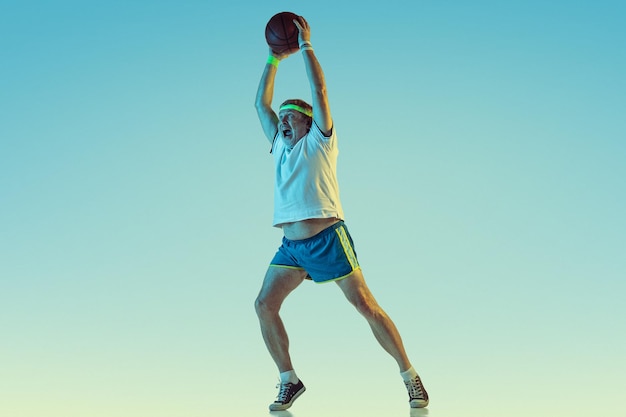 Älterer Mann, der Basketball auf Gradientenhintergrund im Neonlicht spielt. Das kaukasische männliche Model in guter Form bleibt aktiv und sportlich.