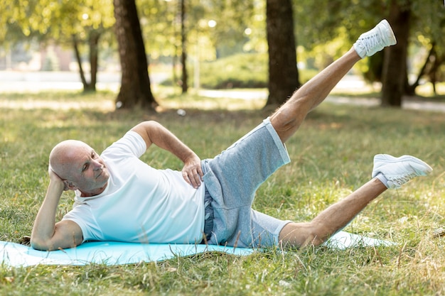 Älterer Mann, der draußen Übungen auf Yogamatte tut