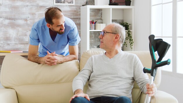 Älterer Mann, der ein Gespräch mit einem Krankenpfleger im gemütlichen Pflegeheim führt.