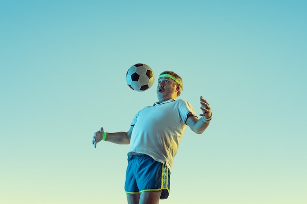 Älterer Mann, der Fußball in Sportbekleidung auf Farbverlauf und Neonlicht spielt