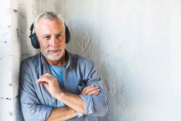 Älterer Mann, der gegen hörende Musik der Wand auf Kopfhörer steht