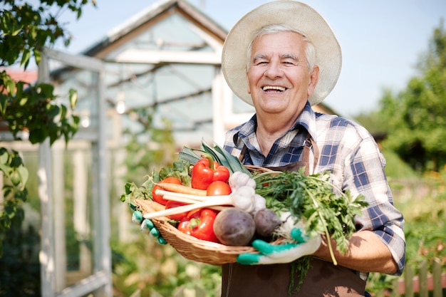 Älterer Mann, der im Feld mit einer Kiste des Gemüses arbeitet