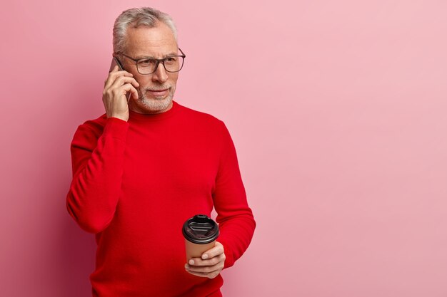 Älterer Mann, der roten Pullover trägt und am Telefon spricht