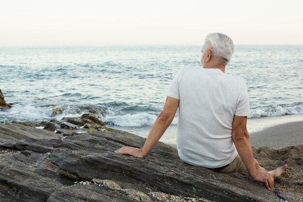 Älterer Mann, der sich am Strand ausruht und das Meer bewundert