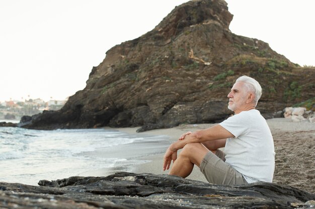Älterer Mann, der sich am Strand ausruht und das Meer bewundert