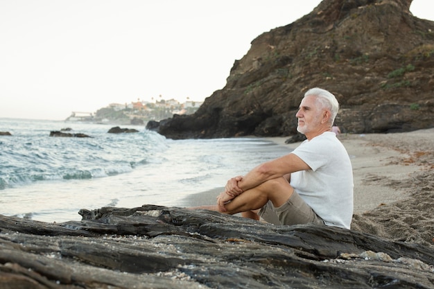 Älterer Mann, der sich am Strand ausruht und das Meer bewundert