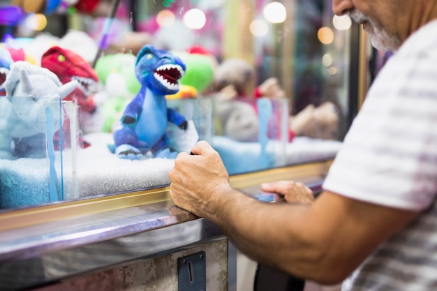 Älterer Mann, der Spielzeuggreifer-Maschine spielt