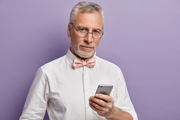 Älterer Mann im weißen Hemd und in der rosa Fliege, die Telefon hält