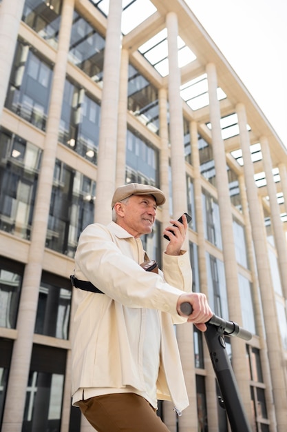 Älterer Mann in der Stadt mit einem Elektroroller mit Smartphone