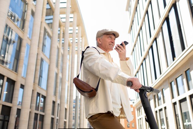 Älterer Mann in der Stadt mit einem Elektroroller mit Smartphone