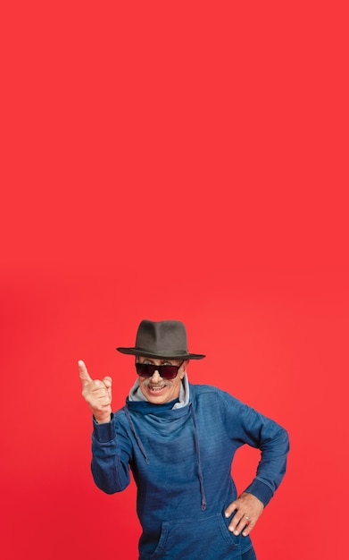 Älterer Mann in stylischen Brillen und Hut isoliert auf Rot