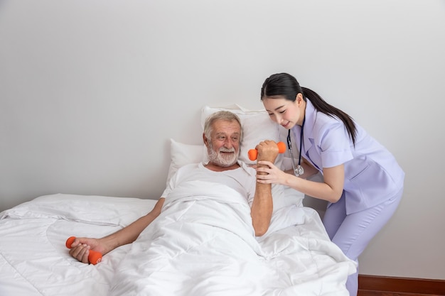 Älterer Mann mit Hanteln mit Physiotherapeut im Schlafzimmer im Pflegeheim