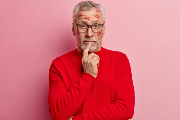 Älterer Mann mit Lippenstiftflecken im Gesicht und mit rotem Pullover