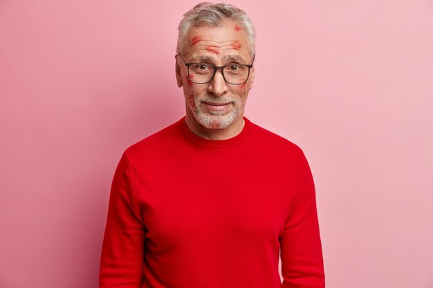 Älterer Mann mit Lippenstiftflecken im Gesicht und mit rotem Pullover