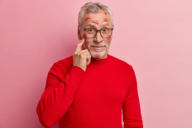 Älterer Mann mit Lippenstiftflecken im Gesicht und mit rotem Pullover