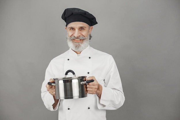 Älterer Mann mit Metallpfanne. Koch in einem schwarzen Hut.