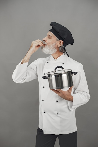 Älterer Mann mit Metallpfanne. Koch in einem schwarzen Hut.