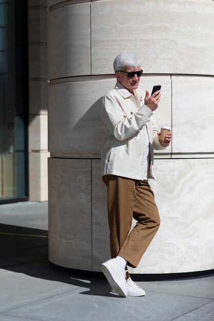 Älterer Mann mit Sonnenbrille im Freien in der Stadt mit Smartphone beim Kaffeetrinken