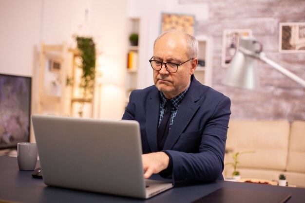 Älterer Mann tippt auf Laptop im gemütlichen Wohnzimmer.