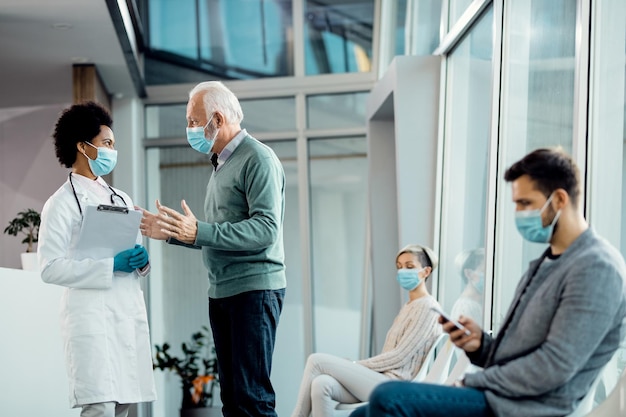 Älterer Mann und afroamerikanischer Arzt tragen Gesichtsmasken, während sie im Krankenhaus sprechen