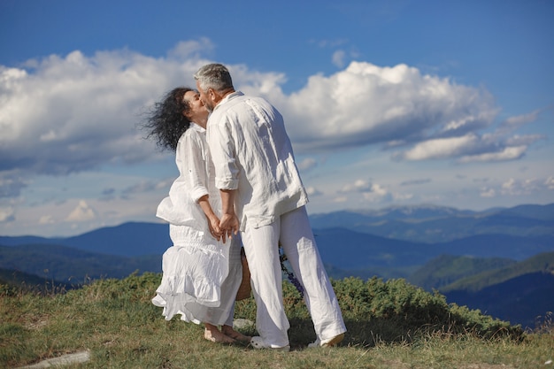 Älterer Mann und Frau in den Bergen. Erwachsenes Paar verliebt in Sonnenuntergang. Mann in einem weißen Hemd.