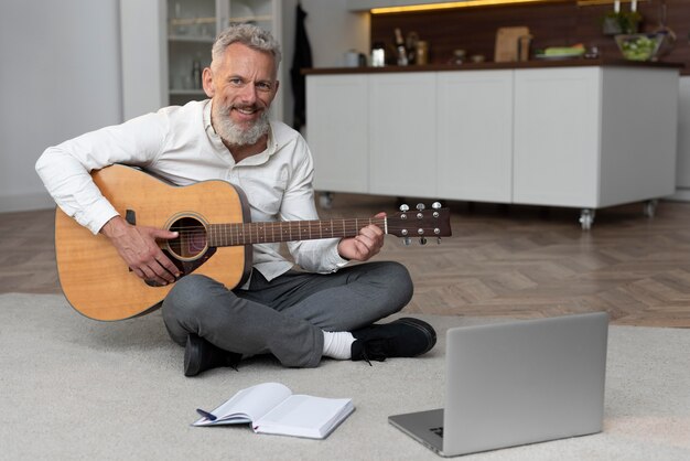 Älterer Mann zu Hause auf dem Boden beim Gitarrenunterricht