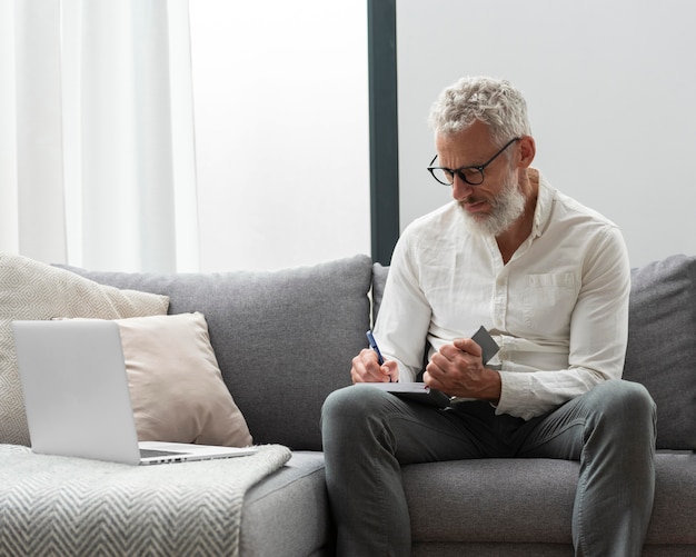 Älterer Mann zu Hause, der am Laptop lernt und Notizen macht