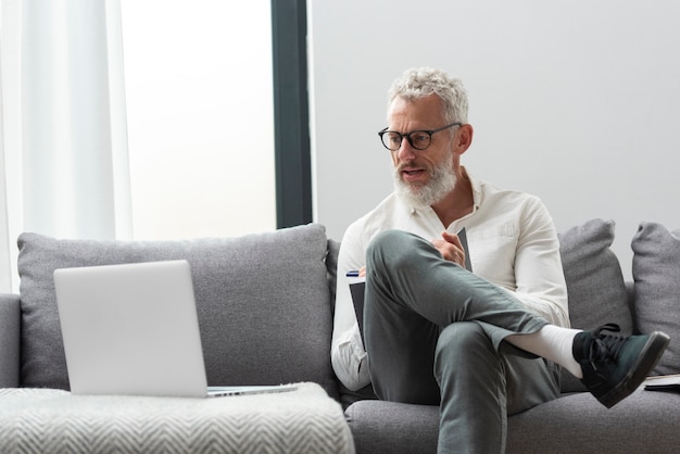 Älterer Mann zu Hause, der am Laptop lernt und Notizen macht