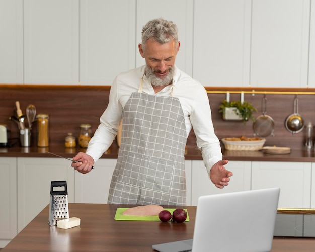 Älterer Mann zu Hause in der Küche, der Kochunterricht auf dem Laptop nimmt