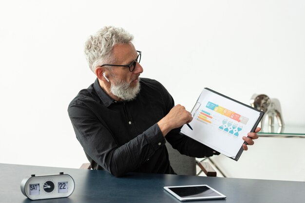 Älterer Mann zu Hause mit Grafik auf Notizblock mit Tablet auf dem Schreibtisch