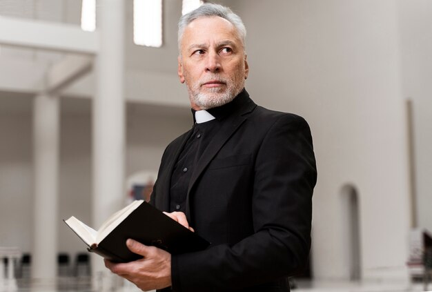 Älterer Priester des mittleren Schusses, der Bibel hält
