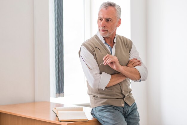 Älterer Professor, der Gläser nahe Schreibtisch im Klassenzimmer hält