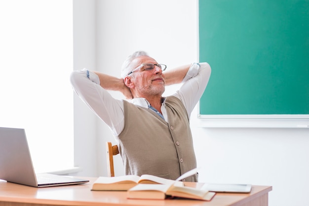 Älterer Professor, der im Klassenzimmer mit den Händen hinter Kopf sitzt