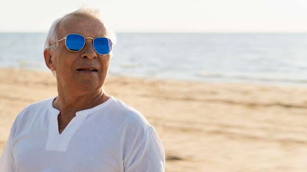 Älterer stilvoller Mann mit Sonnenbrille, die am Strand aufwirft