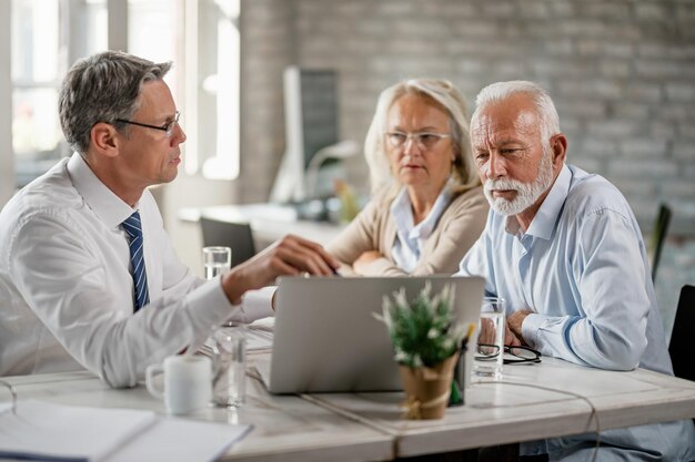 Älteres Ehepaar und sein Bankmanager nutzen Computer, während sie sich im Büro beraten