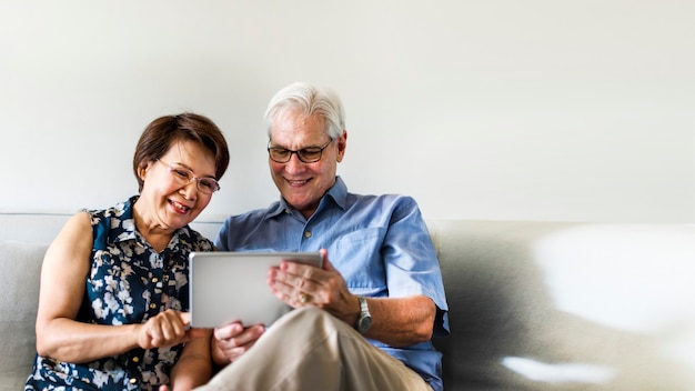 Älteres Paar, das ein digitales Gerät in einem Wohnzimmer verwendet