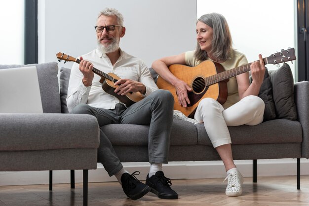 Älteres Paar zu Hause, das Gitarren- und Ukuleleunterricht auf dem Laptop studiert