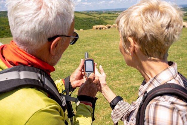 Älteres Wanderpaar, das gemeinsam auf einer Wiese einen Navigator anschaut