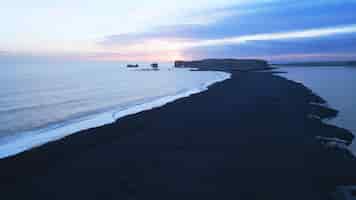 Kostenloses Foto luftansicht auf den schwarzen sandstrand mit bergen und großen steinen in island, wunderschöne natürliche landschaft am strand von reynisfjara. islandische landschaft mit atlantik an der küste.