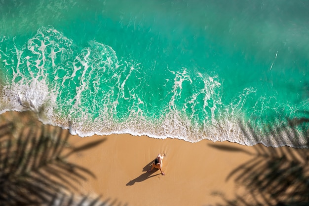 Luftaufnahme der frau sitzt am goldenen sandstrand mit türkisfarbenem meer algarve portugal