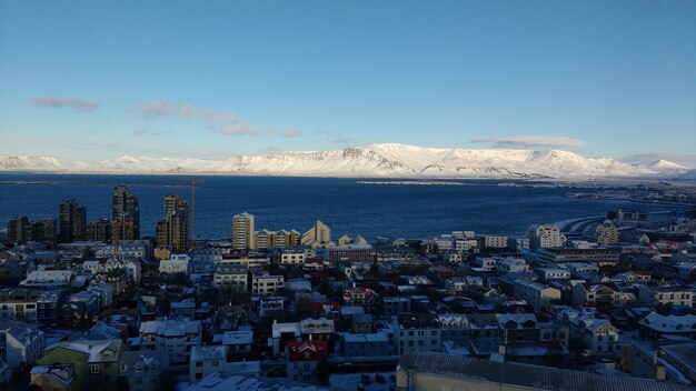 Luftaufnahme der Küstenstadt Reykjavik mit schneebedeckten Bergen gegen einen blauen Himmel