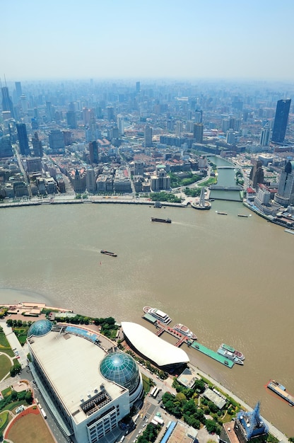 Luftaufnahme der Stadt Shanghai mit städtischer Architektur über Fluss und blauem Himmel am Tag.