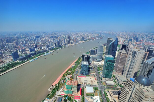 Luftaufnahme der Stadt Shanghai mit städtischer Architektur über Fluss und blauem Himmel am Tag.
