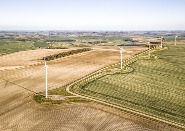 Luftaufnahme der Turbinen auf den schönen grünen Feldern in der Nähe der gepflügten Farmen