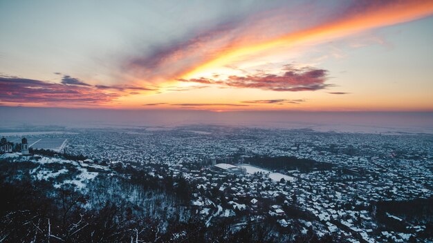 Luftaufnahme eine atemberaubende Sonnenuntergangslandschaft über der Stadt, die im Winter mit Schnee bedeckt wird