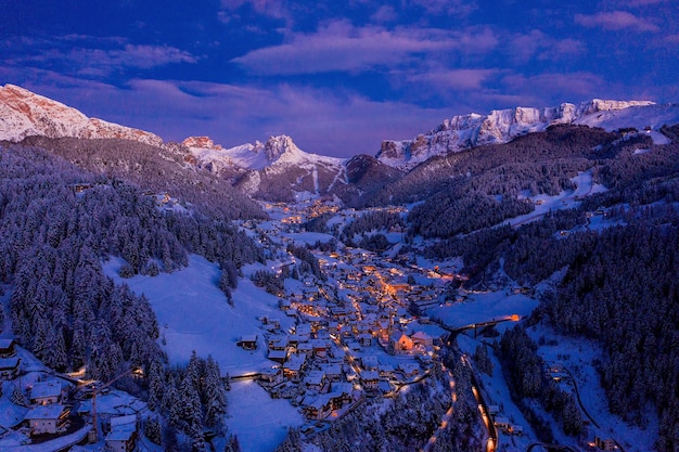 Luftaufnahme einer kleinen hellen Stadt zwischen schneebedeckten Bergen am Abend