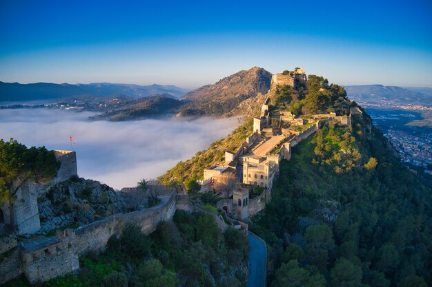Luftaufnahme einer mittelalterlichen Burg auf einem Hügel, die wunderschön mit Nebel bedeckt ist