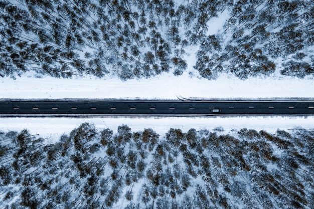 Luftaufnahme einer Straße in einem Wald, der im Winter mit Schnee bedeckt ist