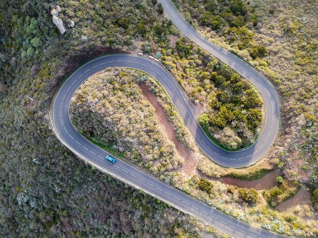 Luftaufnahme eines Autos, das durch eine spiralförmige Straße geht, die durch Bäume in der Landschaft umgeben ist