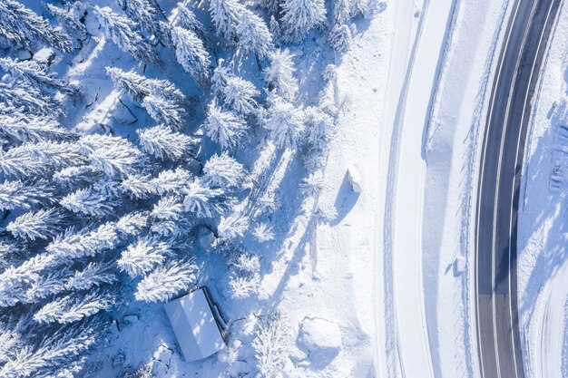 Luftaufnahme eines Waldes mit schneebedeckten Bäumen und einer zweispurigen Straße an der Seite
